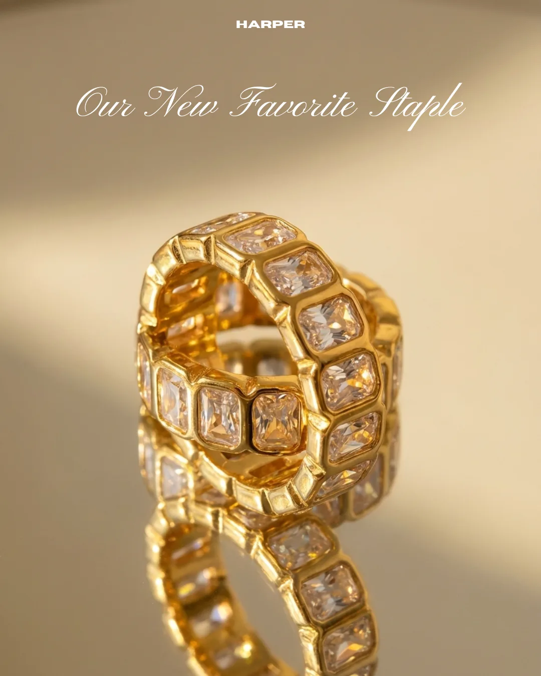 “Our New Favorite Staple” campaign graphic — a gold crystal eternity ring on a mirrored gold ground